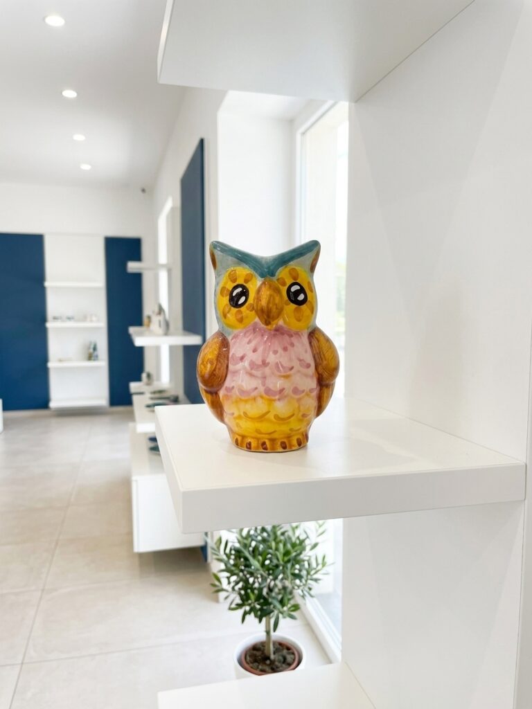 Gufo portafortuna in ceramica colorata su una mensola bianca minimale nello showroom